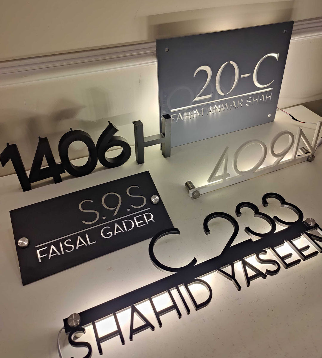 Modern custom house number and name signs displayed on a table, featuring metallic and acrylic finishes, ideal for home and business signage.