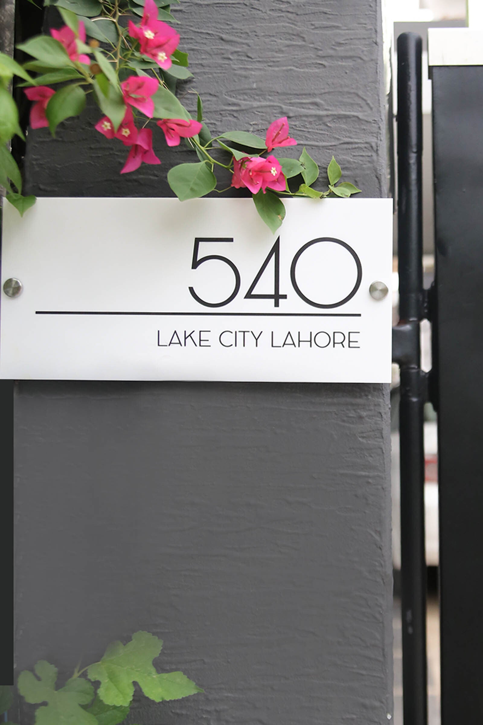 Modern house number plaque 540 Lake City Lahore on a grey wall with pink flowers