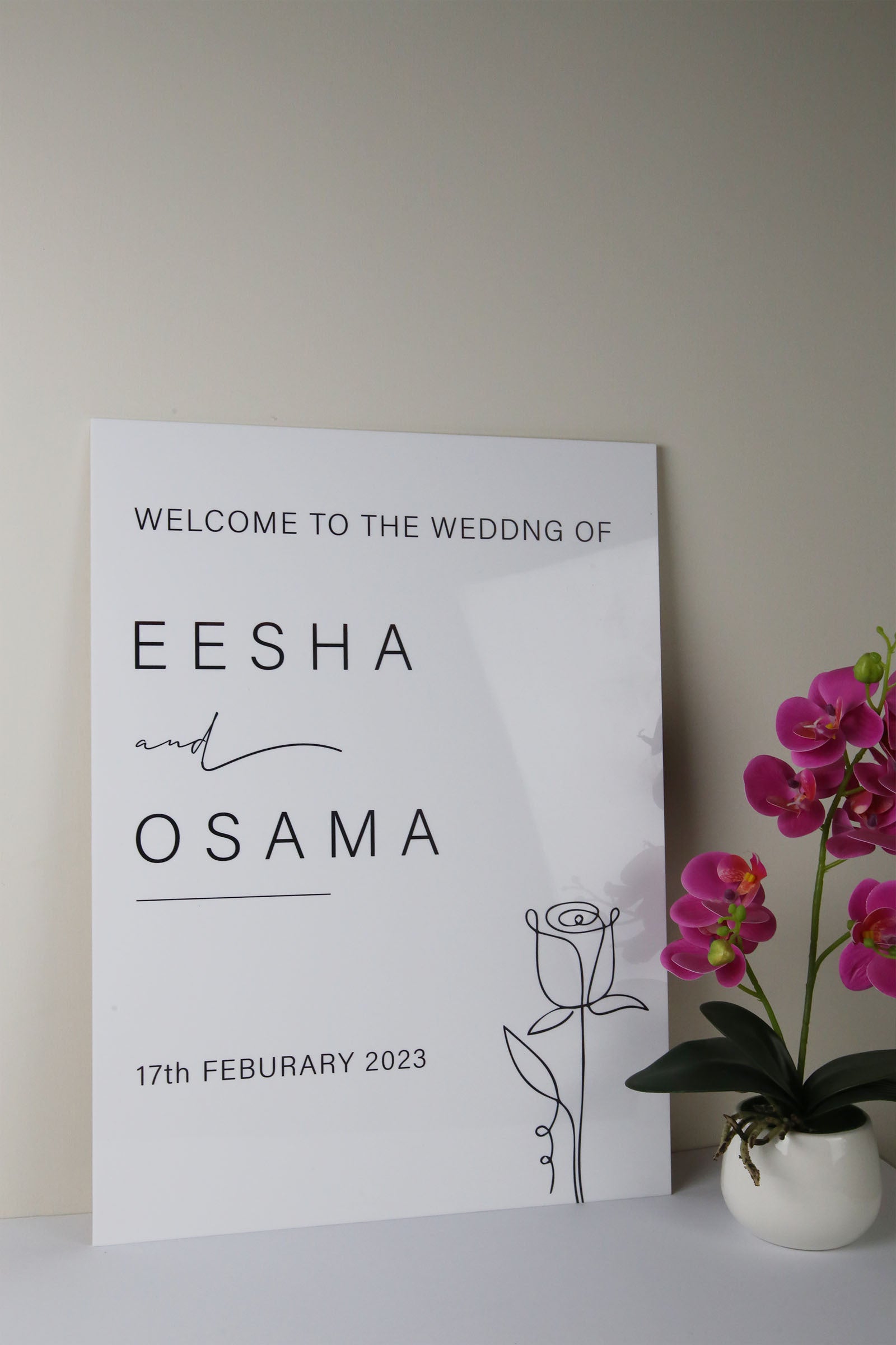 Modern wedding welcome sign with minimalist design, black text, floral illustration, and purple orchid decor
